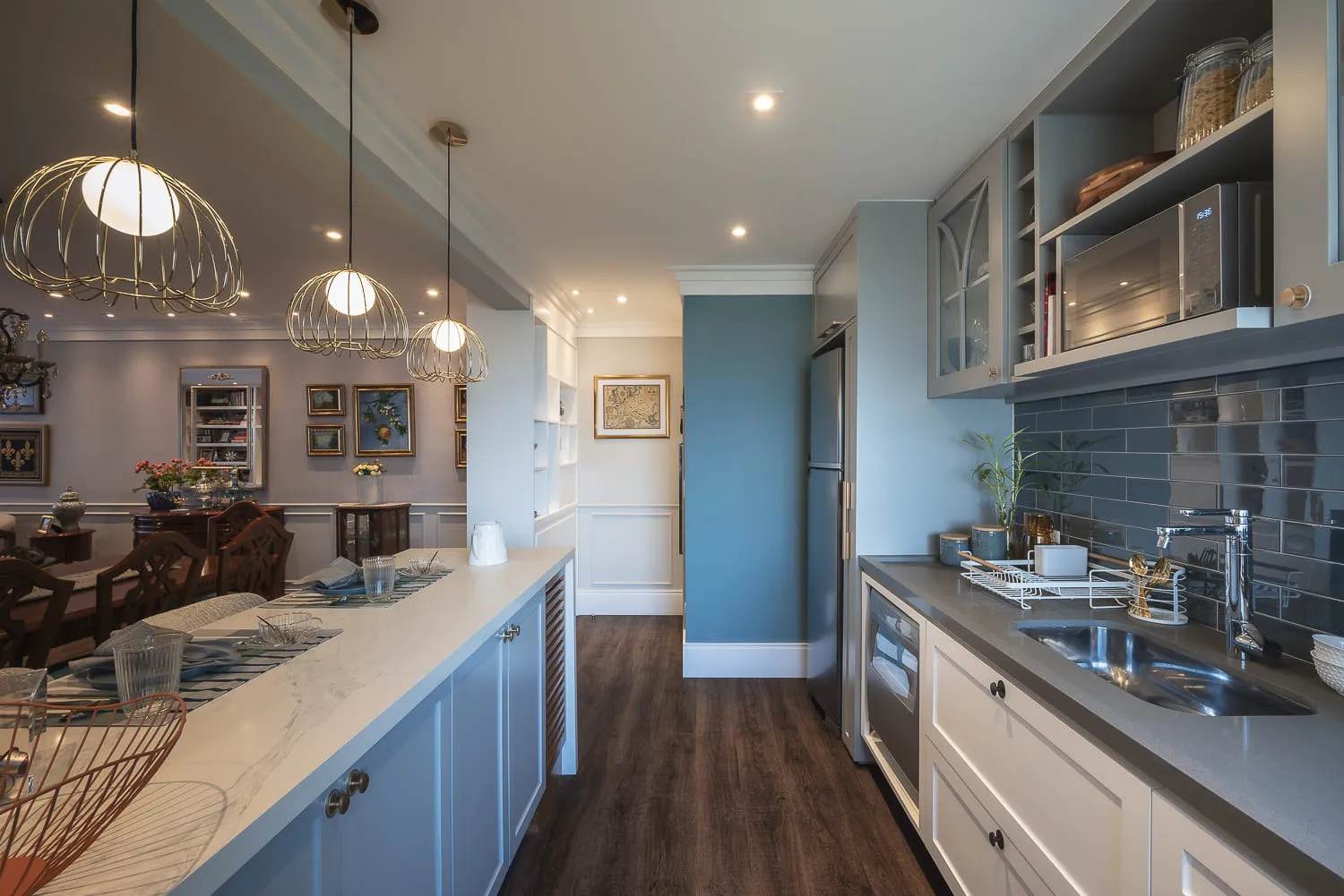 Cozinha integrada à sala de jantar, com pendentes gaiola dourados, bancada de mármore e backsplash de metrô azul