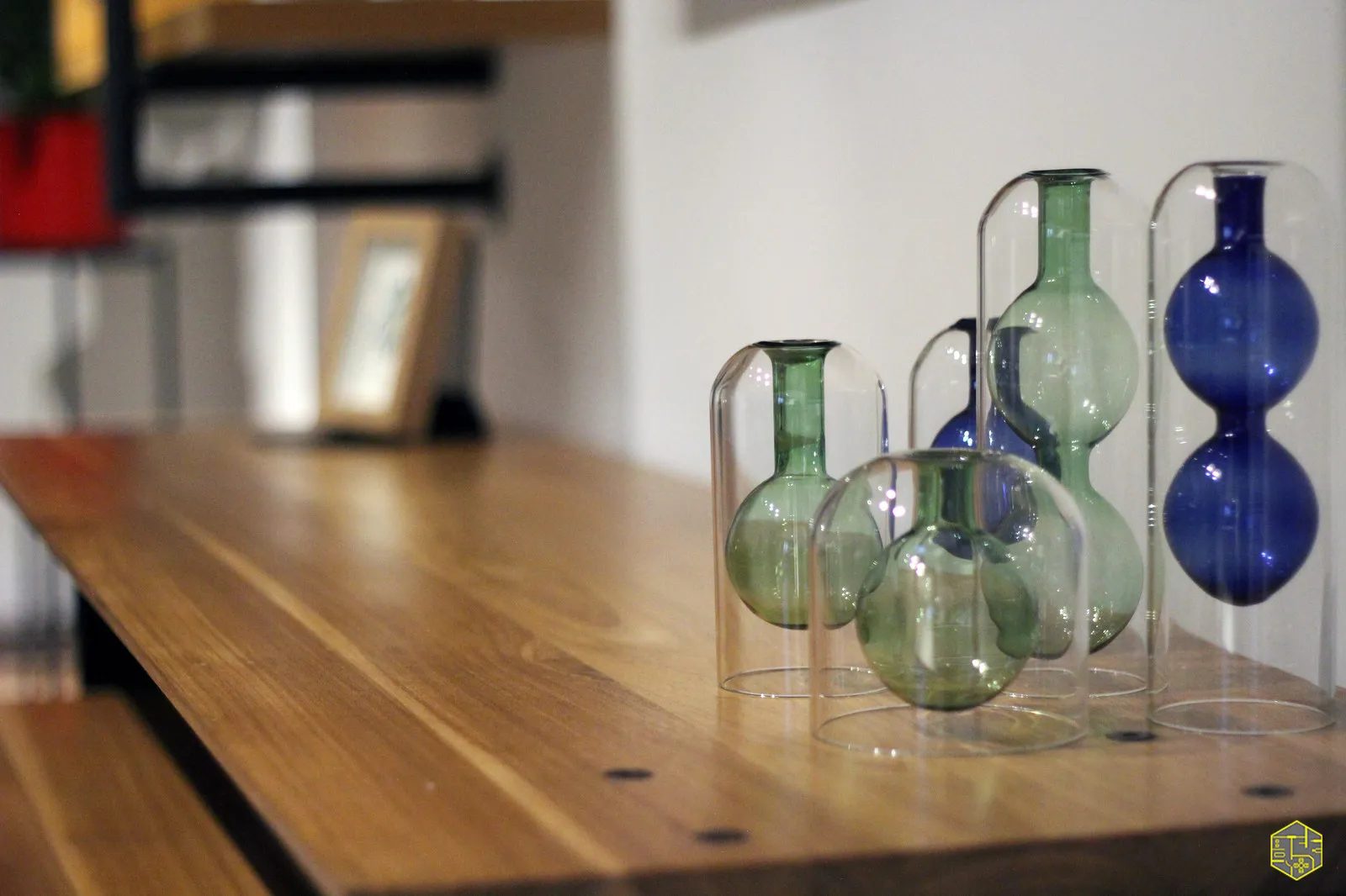Detalhe de vasos de vidro verdes e azuis enfileirados sobre prateleira de madeira