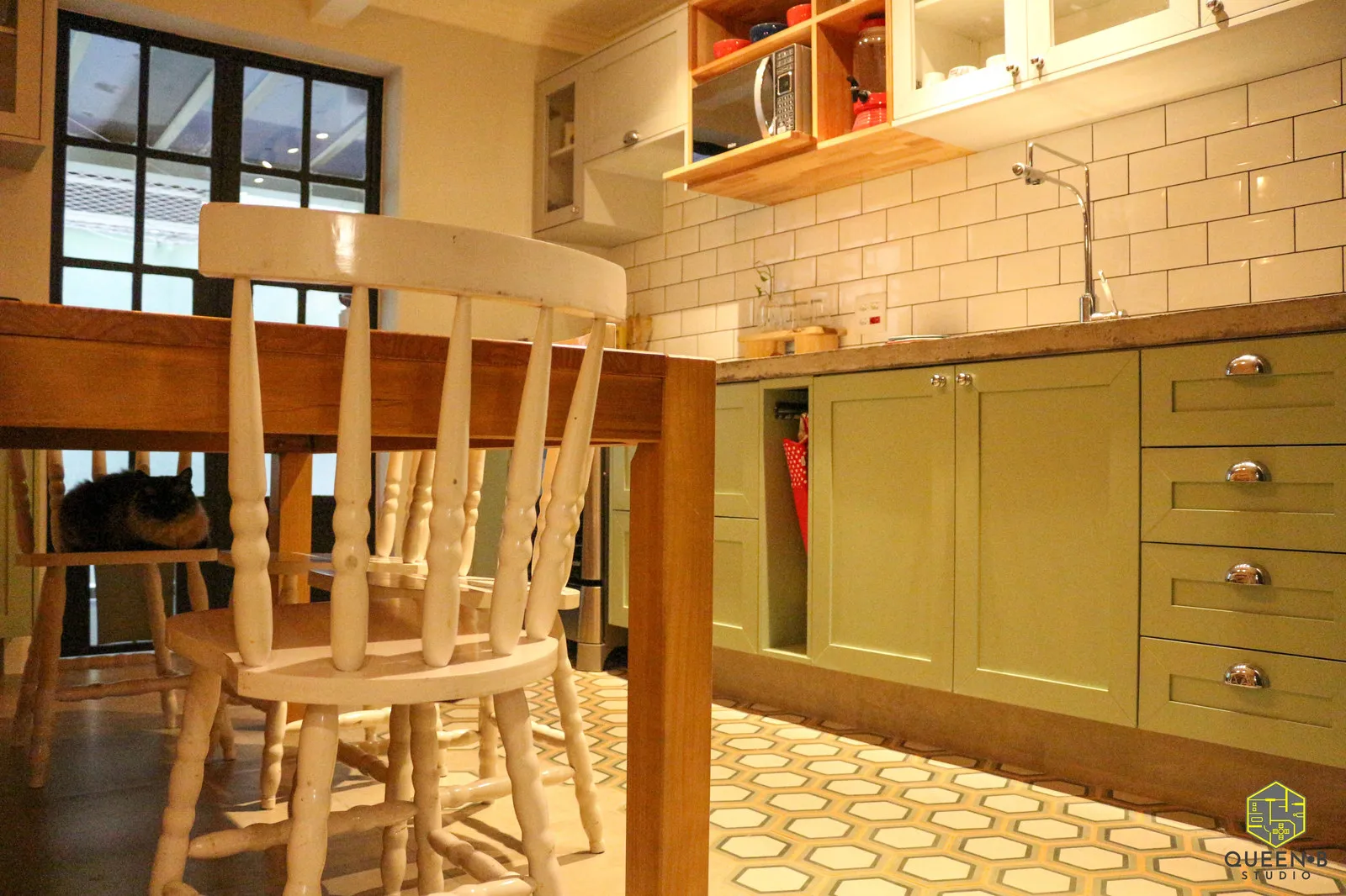 Cozinha com marcenaria verde, azulejo de metrô, piso hidráulico de hexágonos e cadeiras brancas junto à mesa de madeira