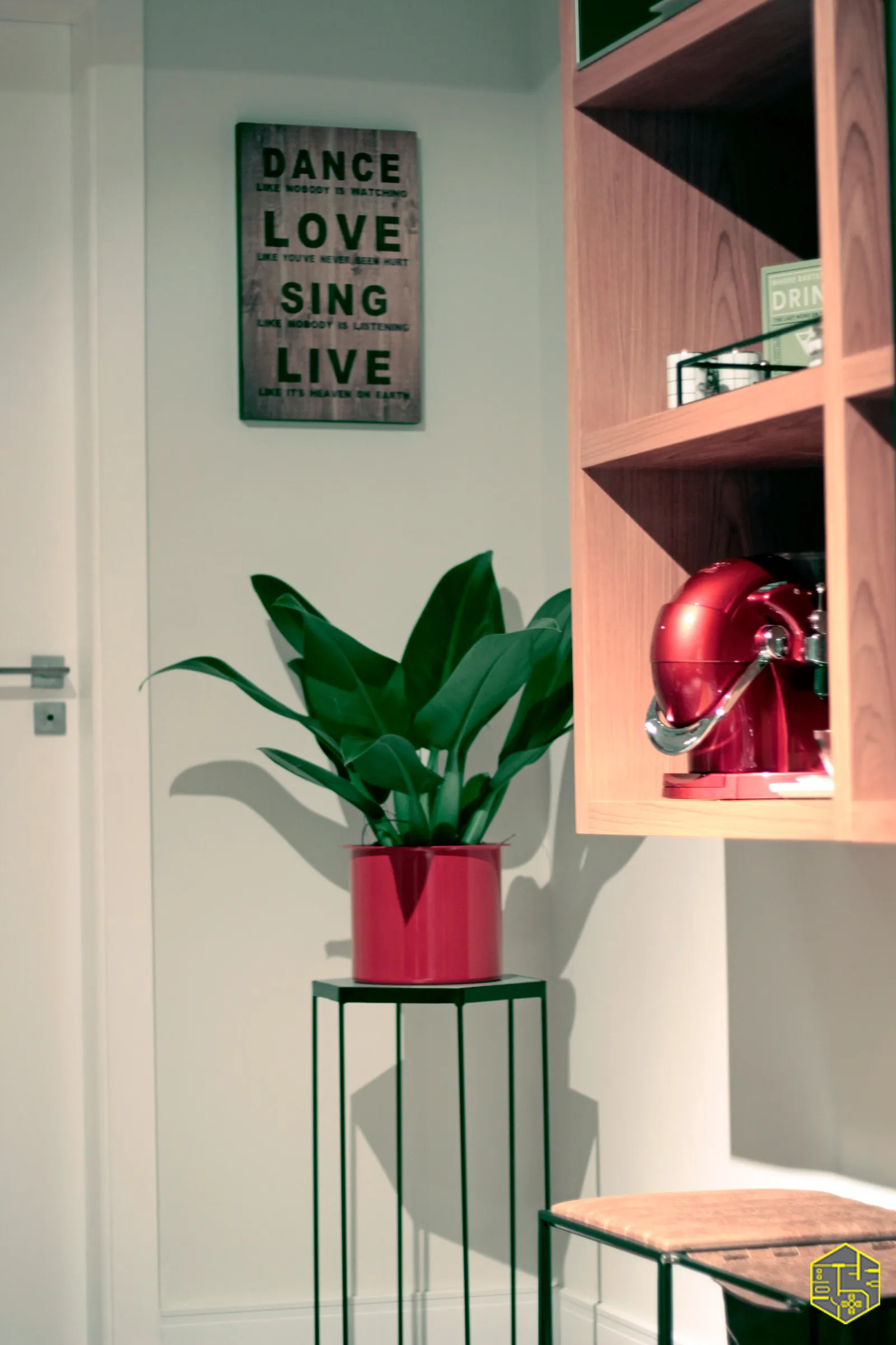 Canto com placa de madeira escrita Dance Love Sing Live, planta em vaso rosa e cafeteira vermelha em nicho de madeira