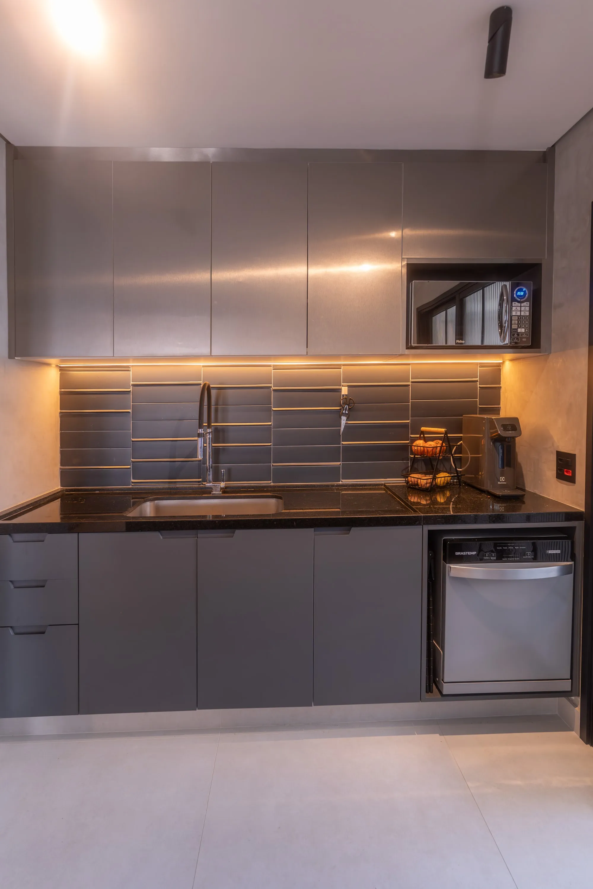 Cozinha com marcenaria cinza, bancada de granito preto, cuba inox e revestimento cinza ripado