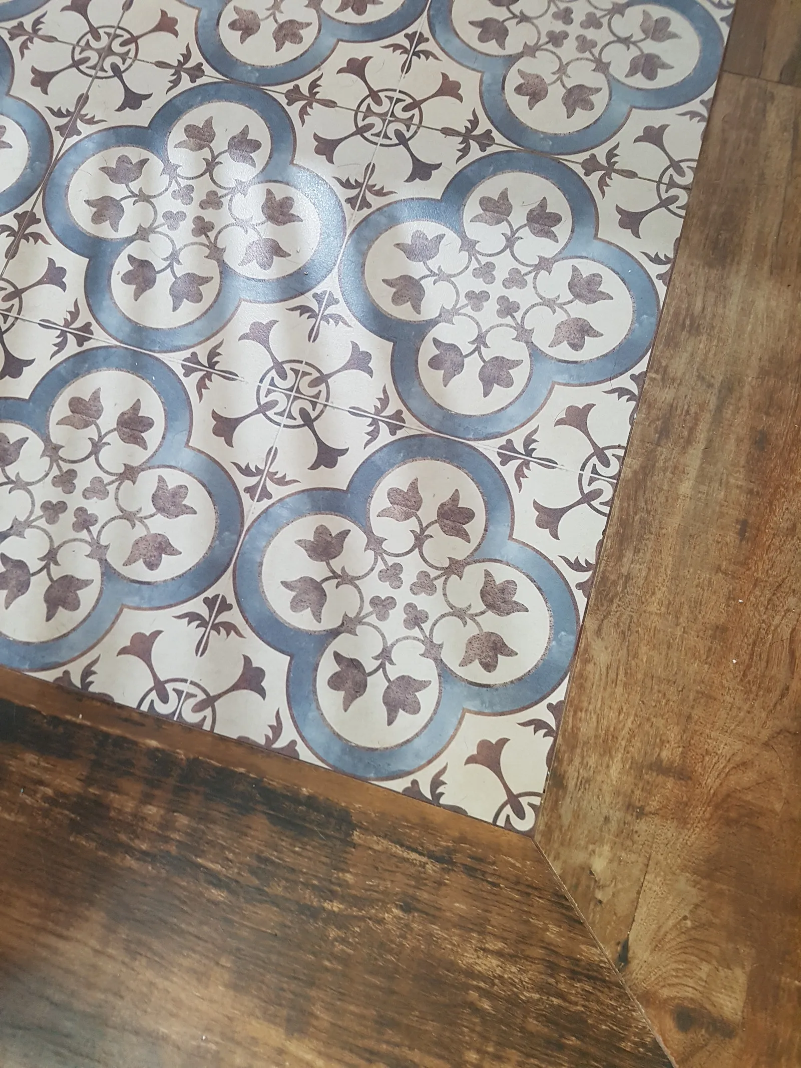 Detalhe do piso de ladrilho hidráulico em azul e marrom encontrando a madeira do piso