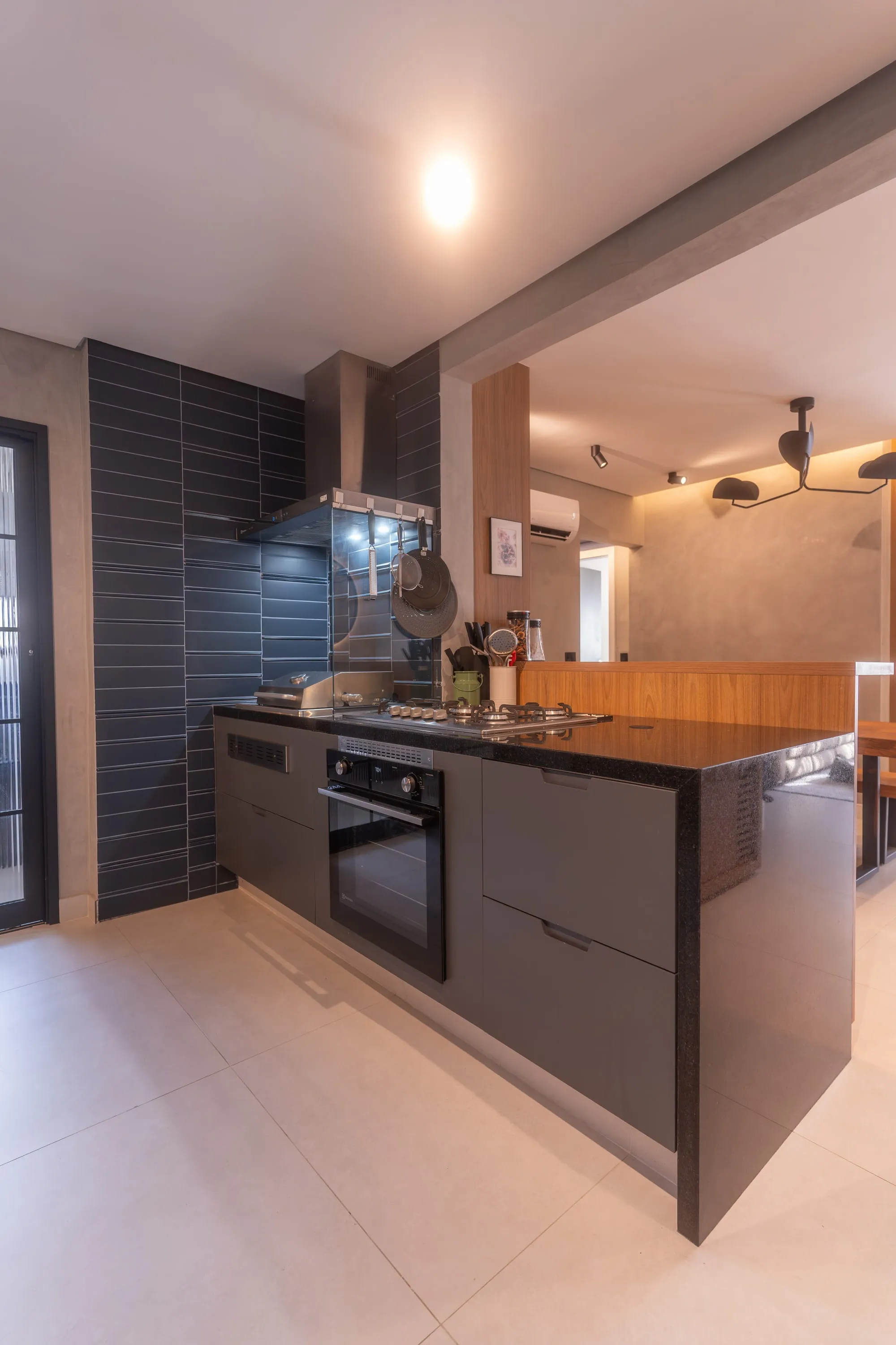 Cozinha com ilha, cooktop, forno embutido, coifa e revestimento preto ripado, integrada à sala de jantar