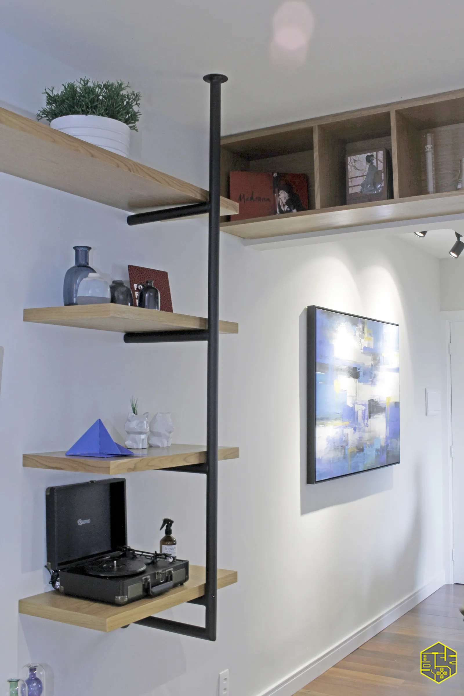 Prateleiras de madeira com estrutura preta de aço, vitrola em maleta, objetos decorativos e quadro abstrato azul na parede