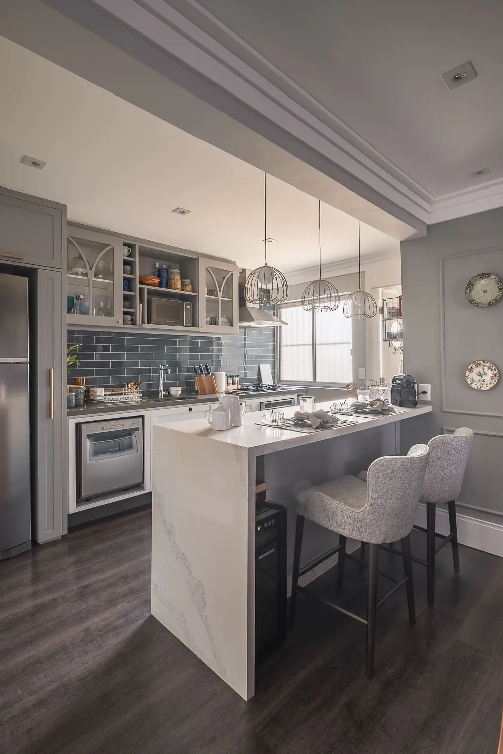 Cozinha com ilha de mármore branco, banquetas cinza estofadas, marcenaria cinza e backsplash de metrô azul