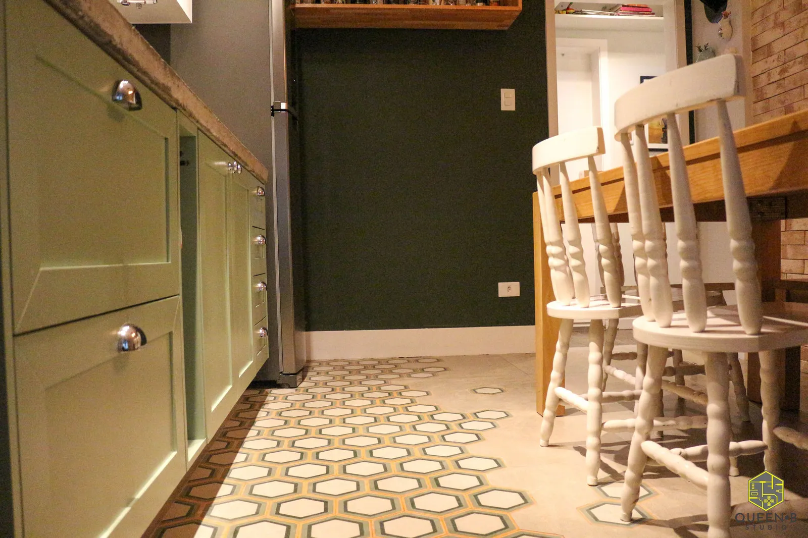 Cozinha com marcenaria verde e puxadores concha cromados, piso de ladrilho hexagonal e cadeiras brancas junto à mesa de madeira