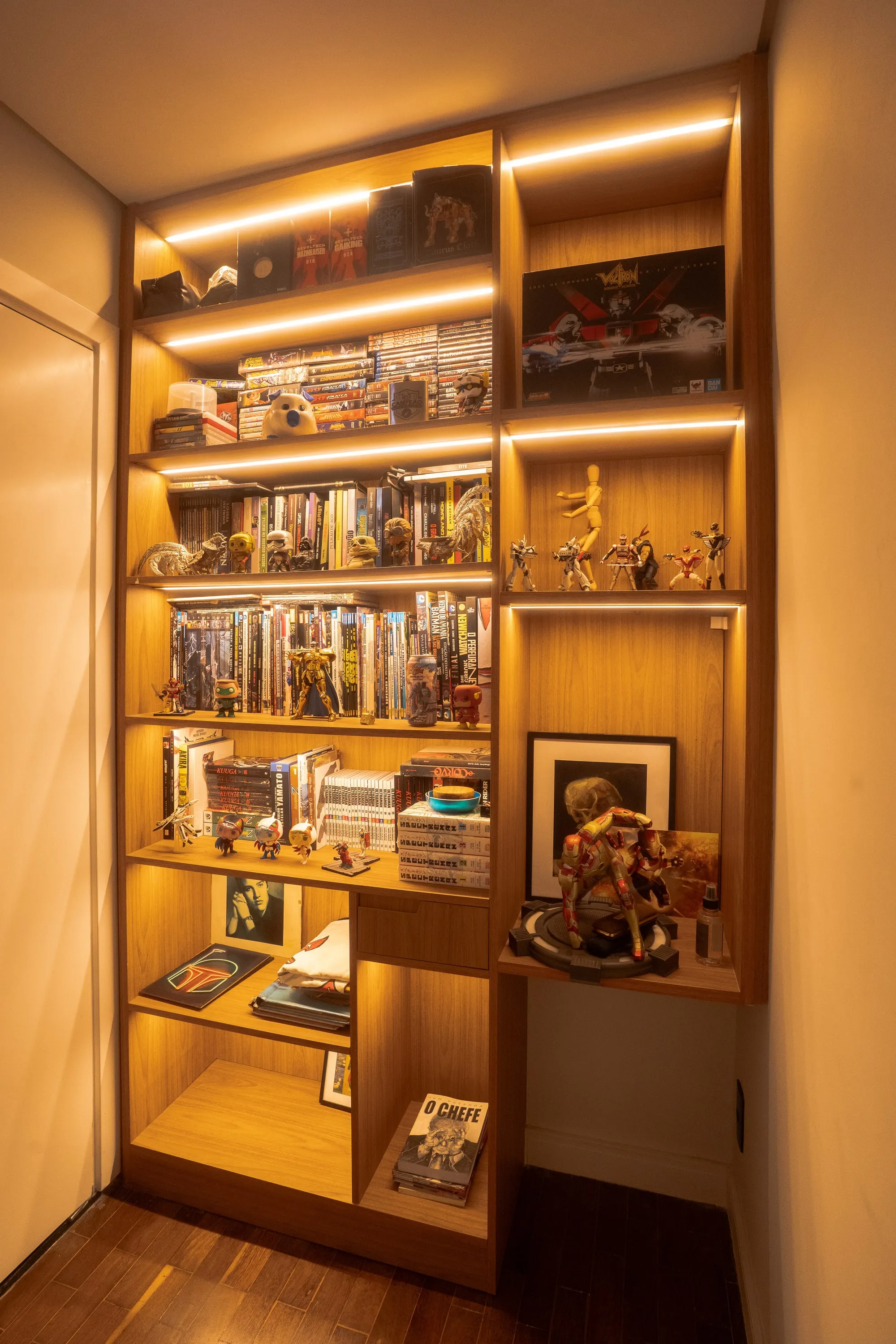 Estante de madeira iluminada com coleção de HQs, action figures e livros