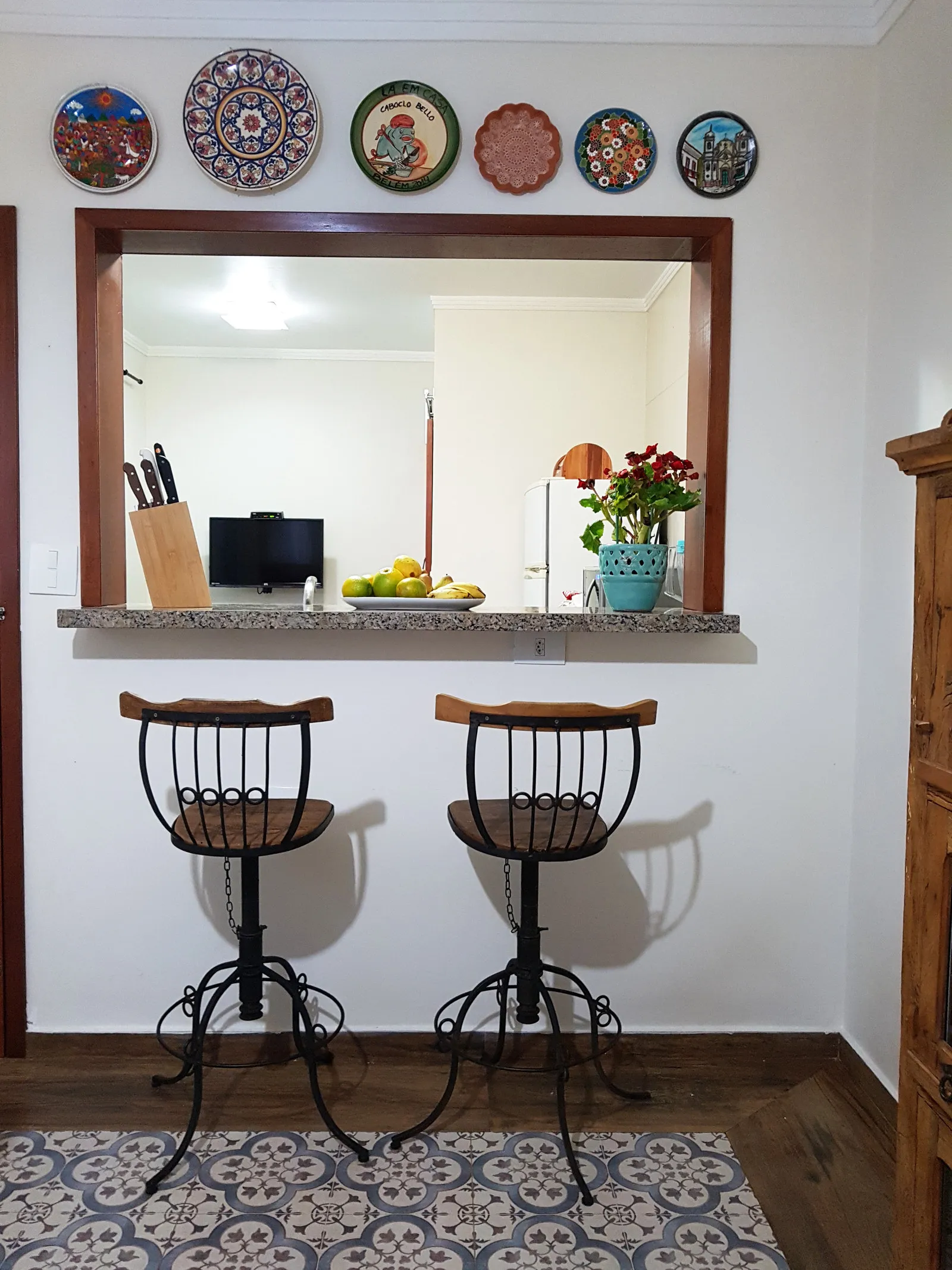Balcão de granito com passa-prates para a cozinha, banquetas de ferro e madeira e pratos decorativos na parede