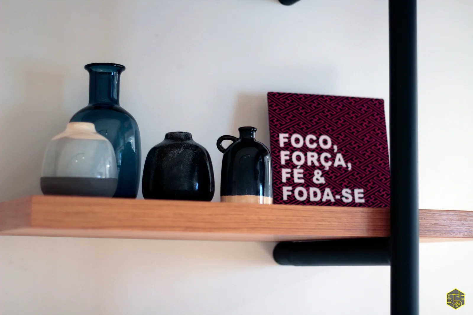 Detalhe de prateleira de madeira com vasos azul e pretos e placa gráfica rosa com frase motivacional