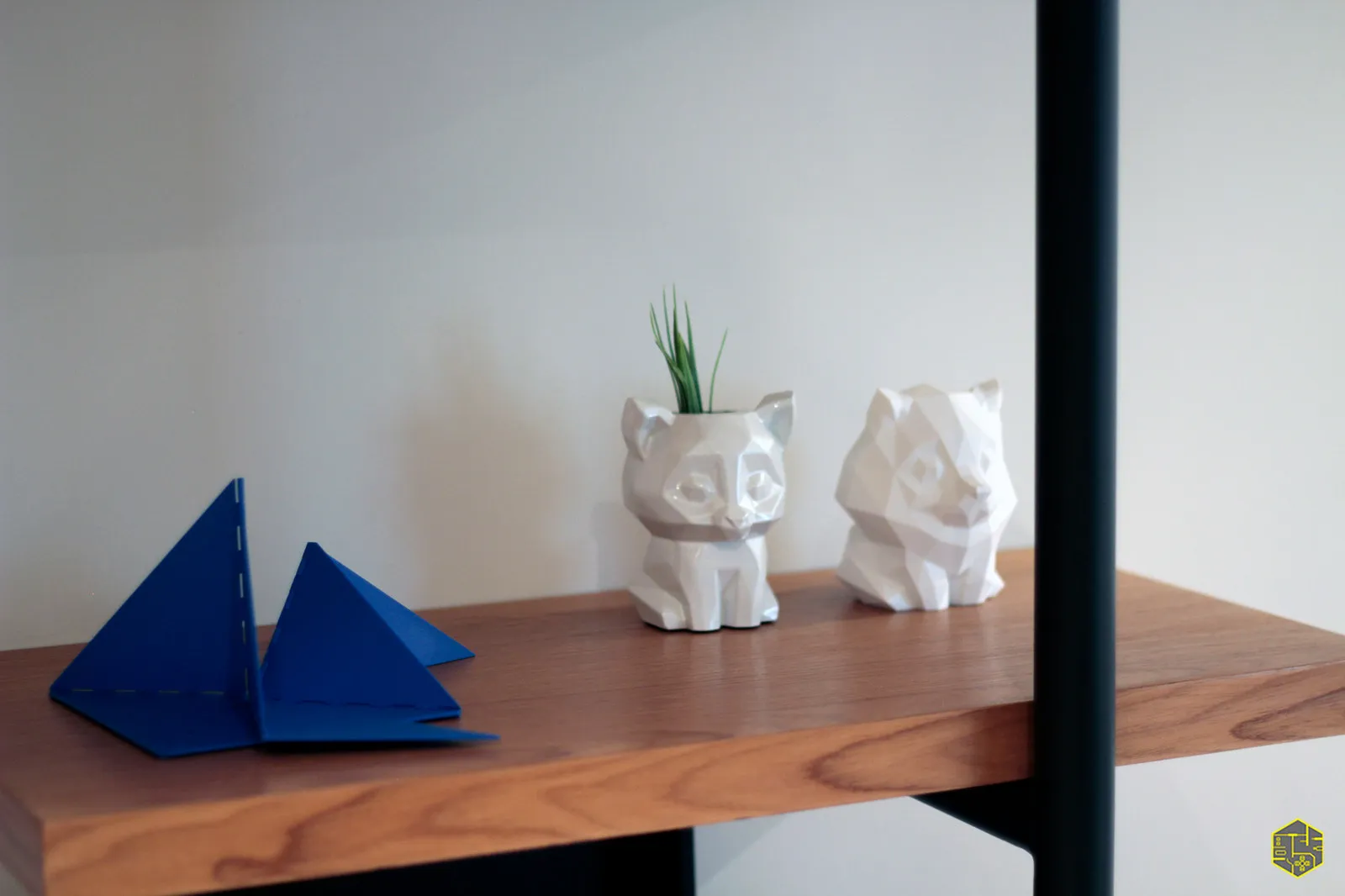 Detalhe de prateleira de madeira com dobradura azul e dois cachepôs brancos geométricos em forma de gato