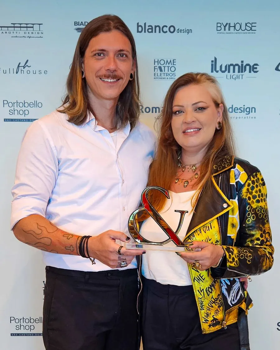Deborah e Juliano com o troféu no painel dos patrocinadores