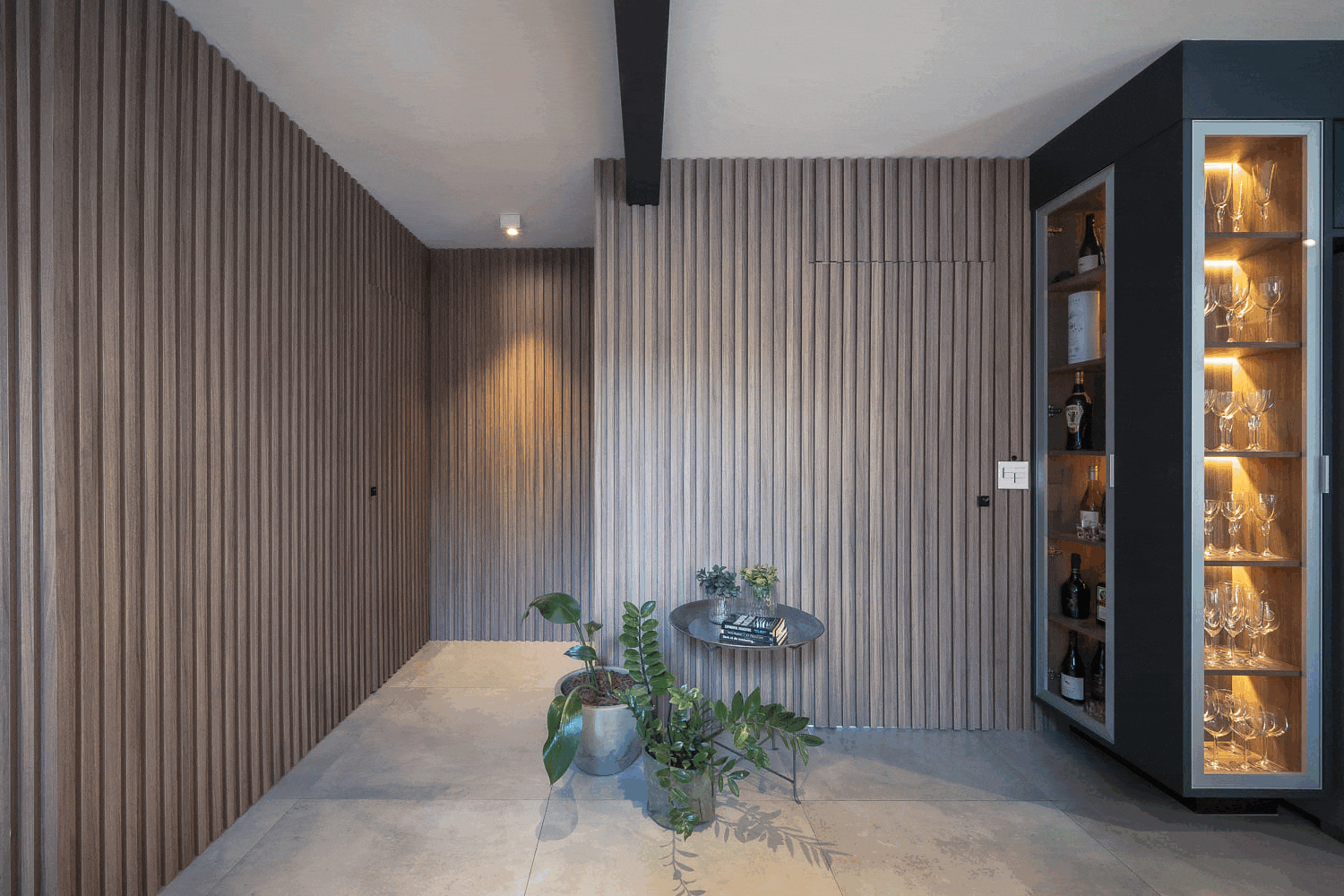 Hall com paredes ripadas de madeira, adega de vidro iluminada e mesa lateral com plantas