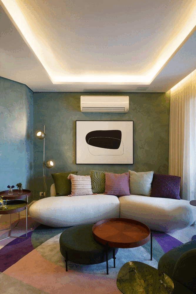 Sala de estar com parede de cimento queimado esverdeado, quadro abstrato, sofá curvo claro de almofadas coloridas e tapete geométrico